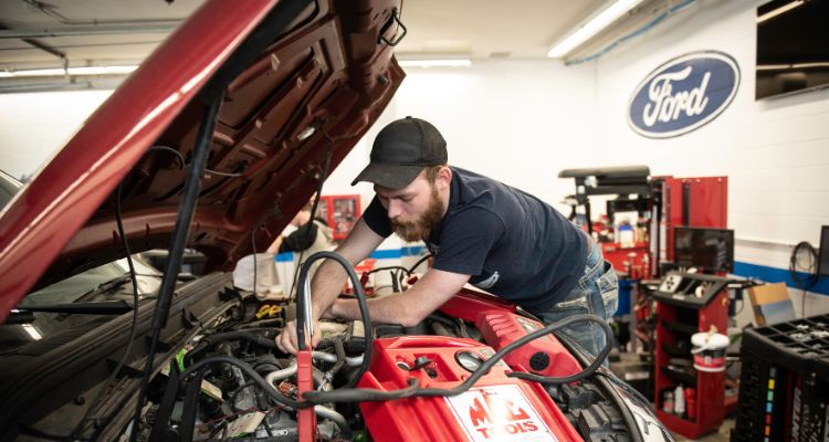 two students and instructor look under the hood of a Ford vehicle