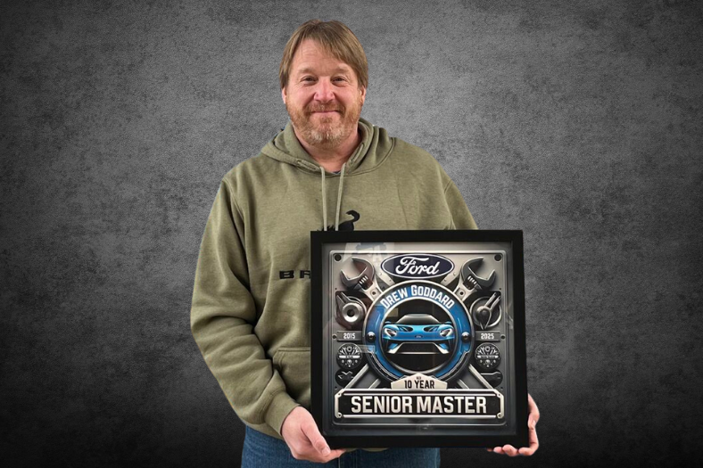 A headshot photo of Drew Goddard holding an award on a gray background.
